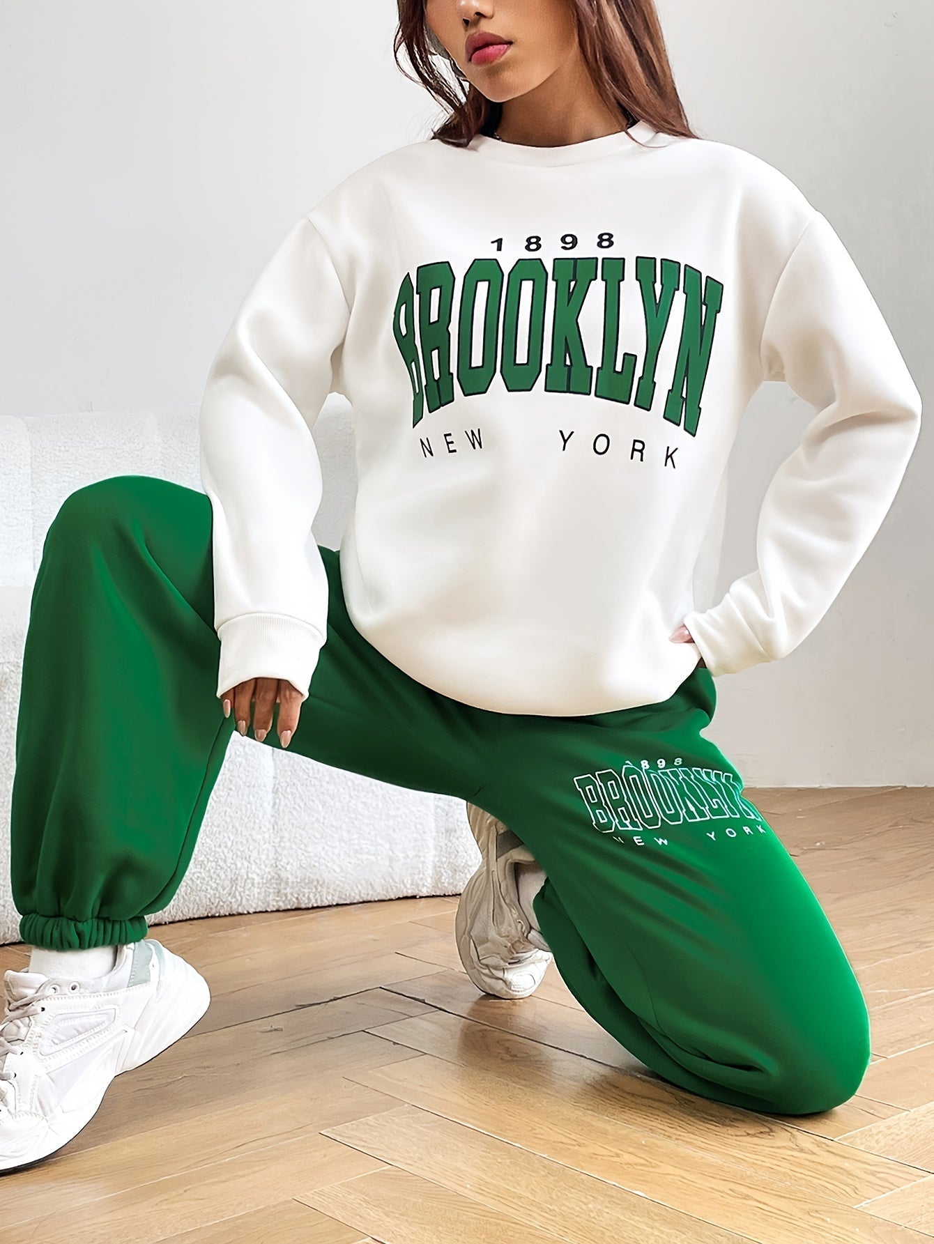 Frau in weißem Brooklyn-Sweatshirt und grüner Jogginghose, lässige Mode, Streetwear-Trend.