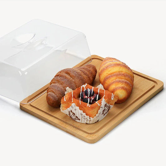Holztablett mit Croissants und Gebäck unter Kunststoffhaube, Frühstück, Bäckerei, Präsentation.