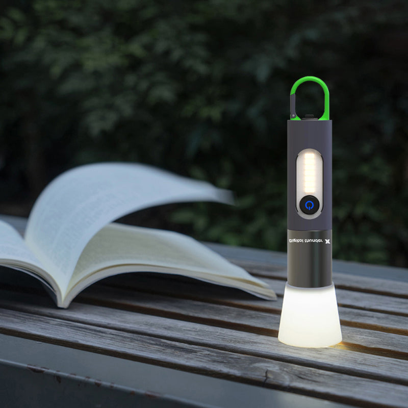 Tragbare LED-Lampe, schwarz, mit Haken, auf Holztisch neben offenem Buch im Freien.