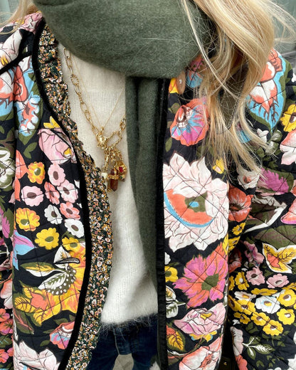 Frau in bunter Blumenjacke und grünem Schal, goldene Kette, modisches Herbstoutfit.