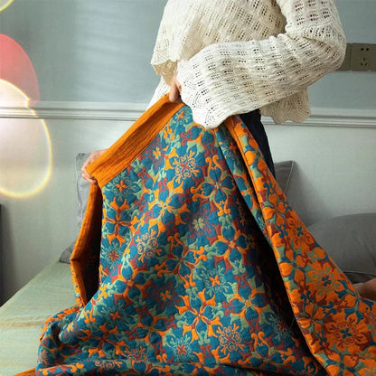 Frau mit bunter, floraler Decke aus Baumwolle auf Sofa, orange-blaues Muster, gemütlich.