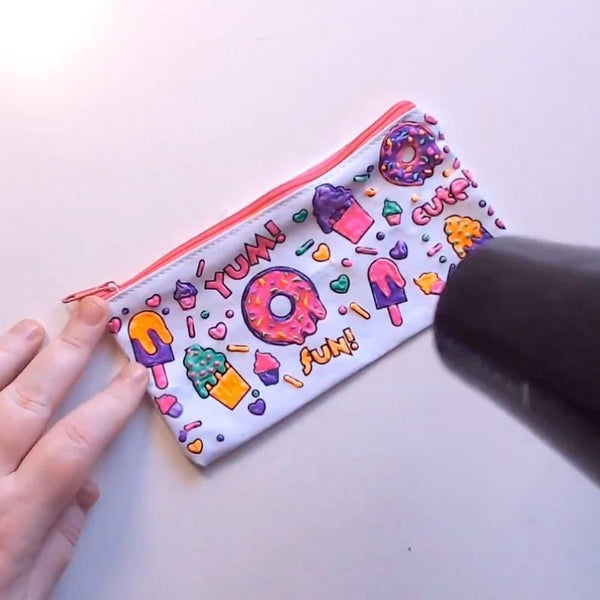 Bunte Kosmetiktasche mit Donut- und Eiscreme-Motiven, Reißverschluss, Hand hält Föhn.