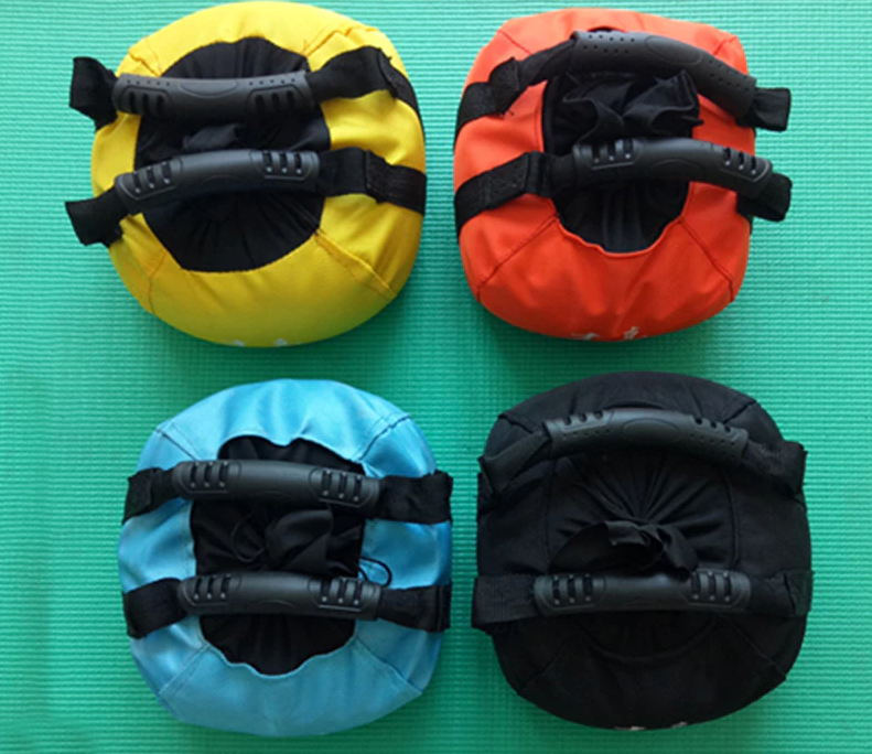 Vier bunte Sandbags mit Griffen auf grüner Matte, Fitness, Training, Gewichte.