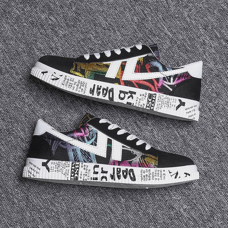 Schwarze Sneaker mit buntem Graffiti-Design und weißer Sohle auf grauem Hintergrund.