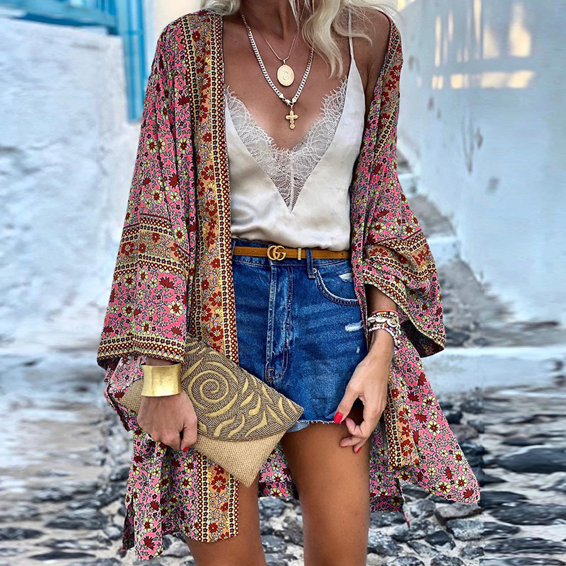 Frau in bunter Kimono-Jacke, Spitzen-Top, Jeansshorts, mit goldener Clutch und Schmuck.