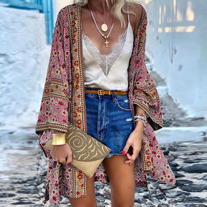 Frau in bunter Kimono-Jacke, Spitzen-Top, Jeansshorts, mit goldener Clutch und Schmuck.