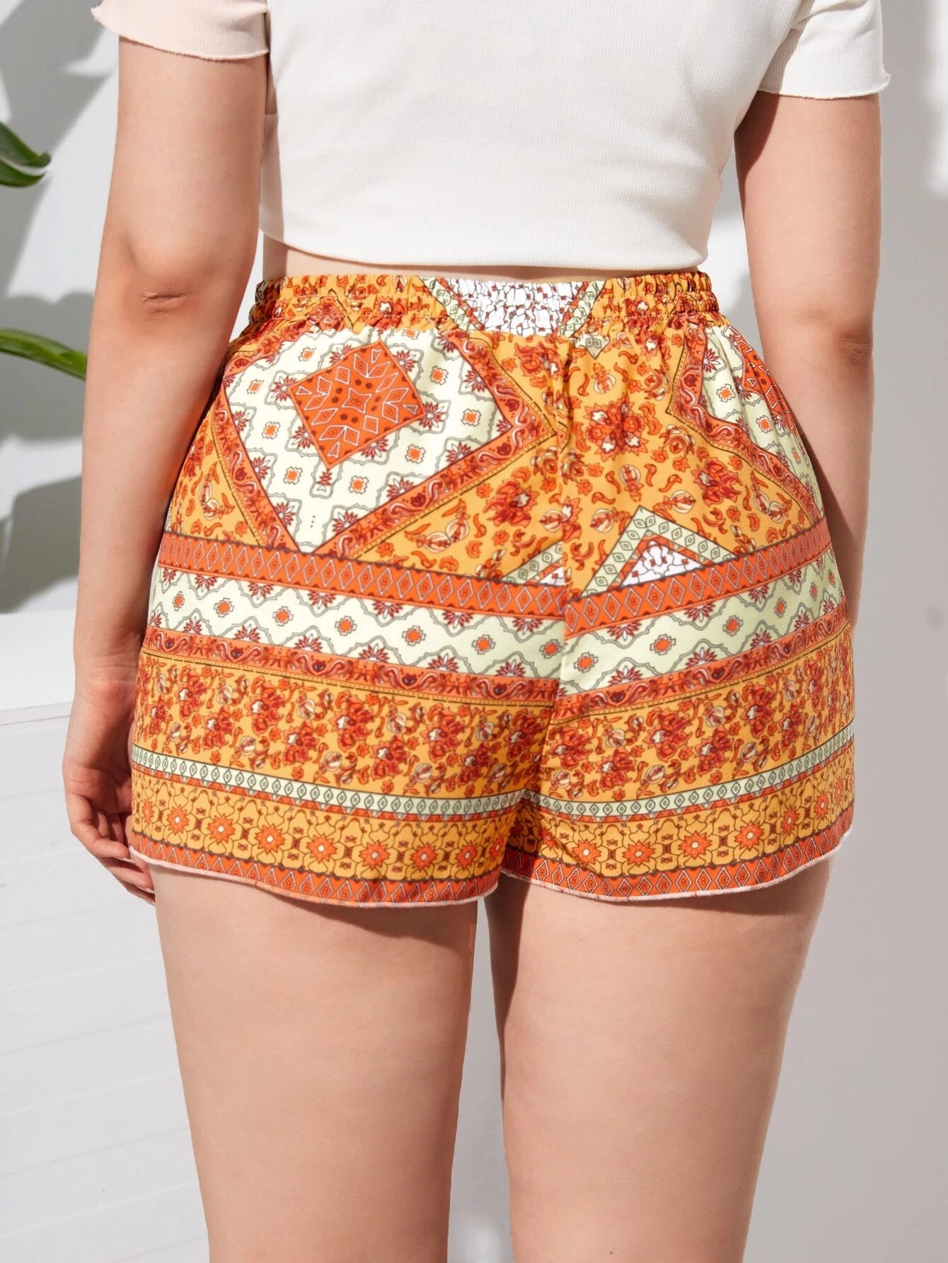 Frau in orange-gemusterten Shorts, Sommermode, Boho-Stil, Baumwolle, Rückansicht.