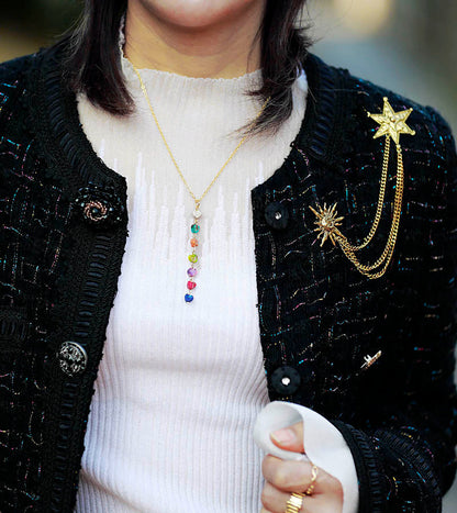 Frau mit schwarzer Jacke, goldener Halskette und Brosche mit Sternmotiv, modisches Accessoire.