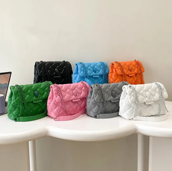 Bunte gesteppte Handtaschen mit Kettenriemen auf Tisch, verschiedene Farben, modisch, Damenaccessoire.