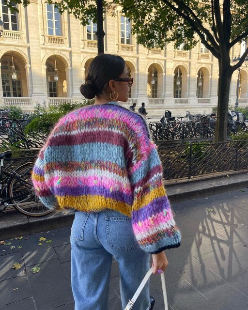 Frau in bunter Strickjacke und Jeans, spaziert in der Stadt, Herbstmode, lässiger Stil.