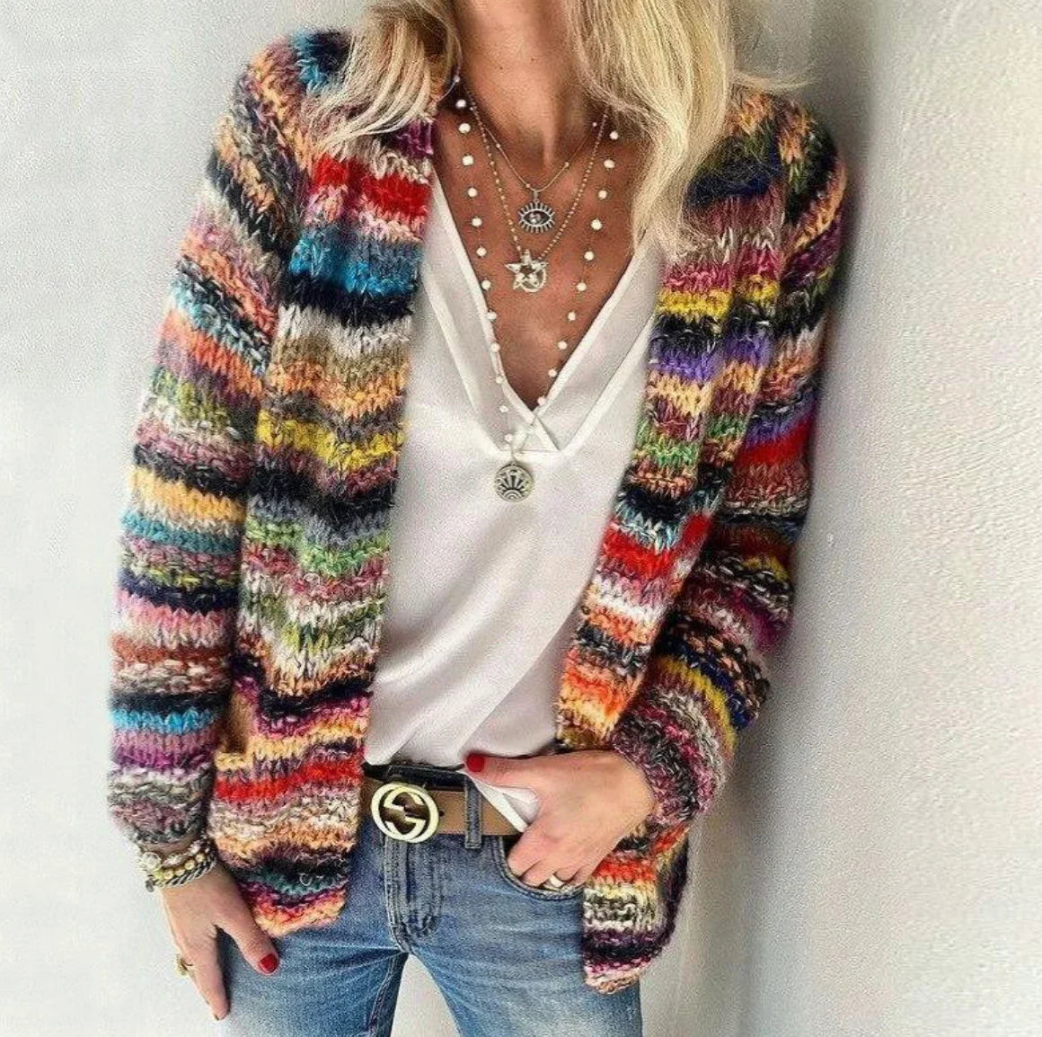 Frau mit buntem Strickcardigan, weißem V-Ausschnitt-Top, Jeans und Schmuck.