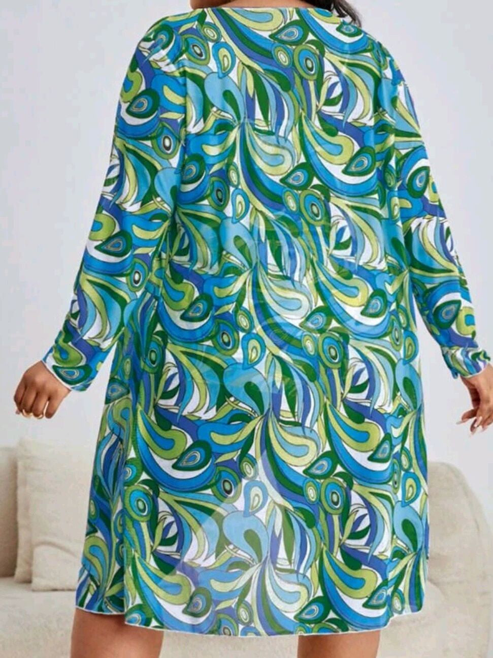 Frau in buntem, langärmligem Kleid mit blau-grünem Paisley-Muster, Rückansicht.