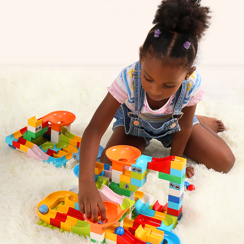 Mädchen spielt mit buntem Murmelbahn-Set auf Teppich, Lernspielzeug, Kinder, Kreativität.