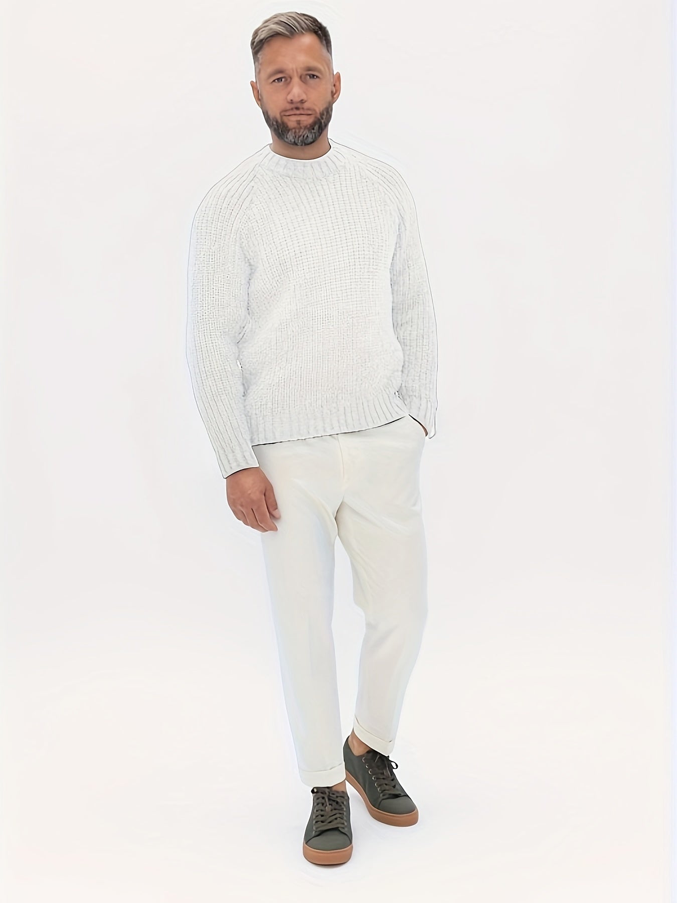 Mann in weißem Strickpullover und Hose, grüne Sneaker, modisches Herrenoutfit.