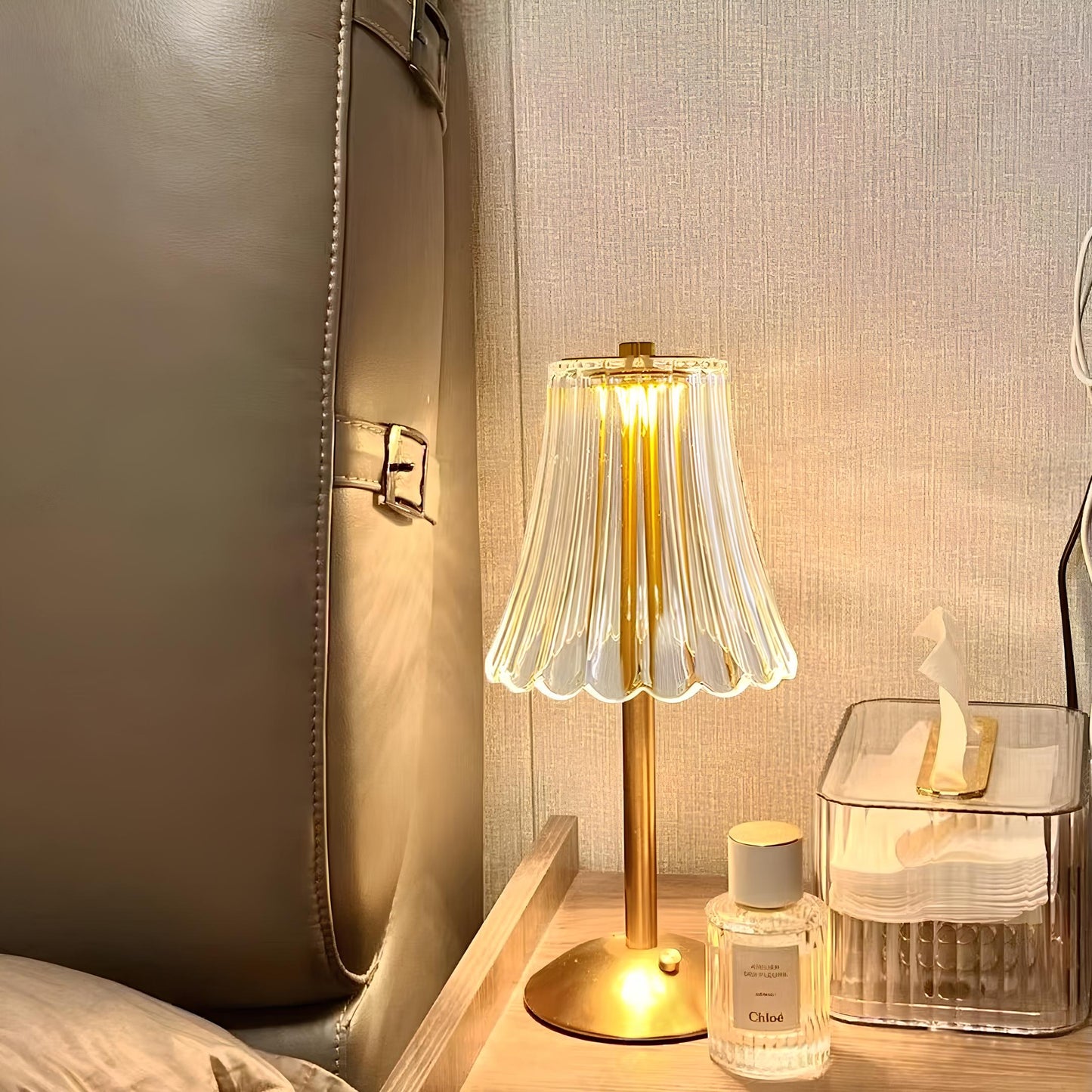 Goldene Tischlampe mit Glaslampenschirm neben Parfümflasche und Taschentuchbox auf Nachttisch.