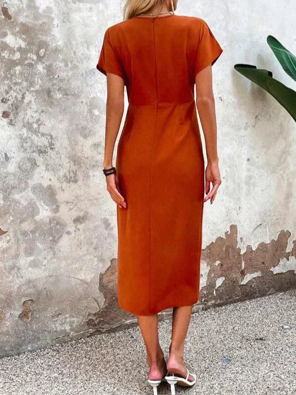 Frau in orangefarbenem Sommerkleid aus Baumwolle, Rückansicht, vor rustikaler Wand.