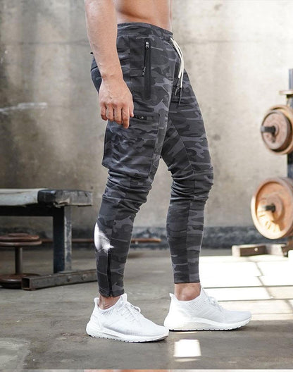 Mann in grauer Camouflage-Trainingshose und weißen Sneakers im Fitnessstudio.
