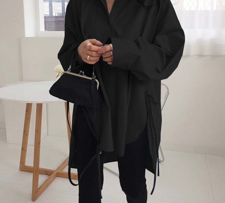 Frau in schwarzer Oversize-Bluse mit kleiner schwarzer Tasche, moderne Mode, minimalistisch.