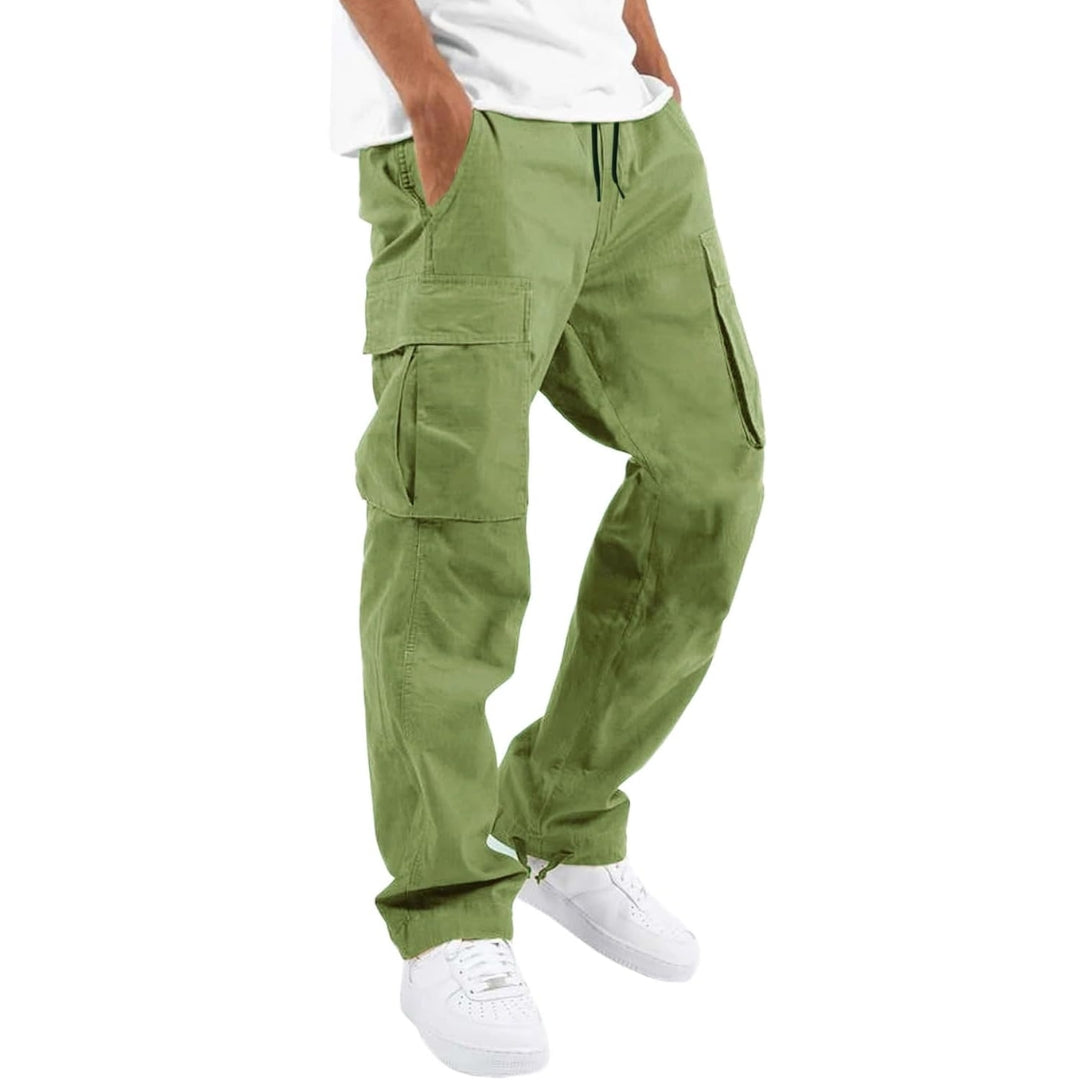 Man bär ljusgröna cargobyxor med sidfickor och dragsko i midjan, vit t-shirt och vita sneakers, hand i fickan. 9
