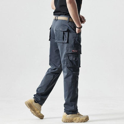 Mann in grauer taktischer Hose mit Seitentaschen, beige Stiefel, Outdoor-Bekleidung.
