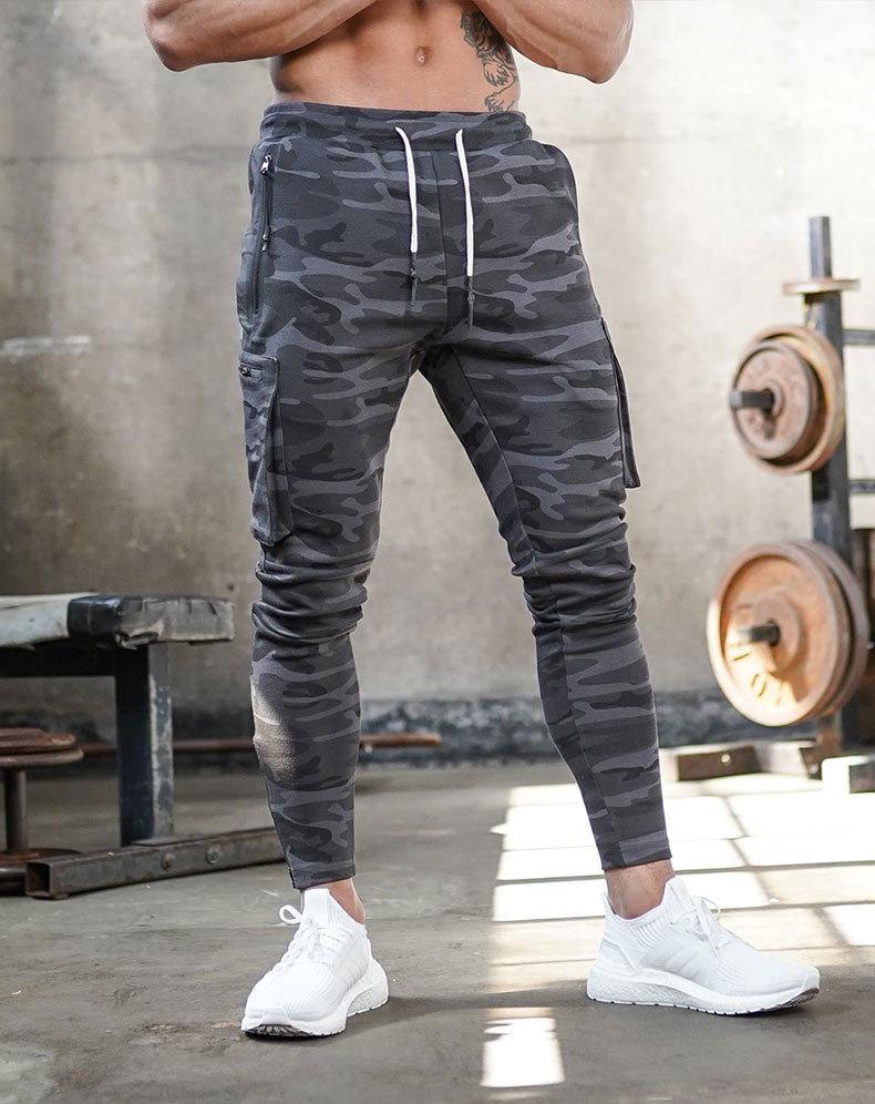 Mann in grauer Camouflage-Trainingshose und weißen Sneakers im Fitnessstudio.