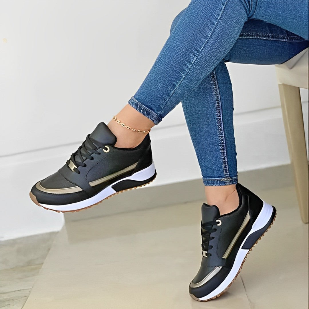 Frau trägt schwarze Sneaker mit goldenen Akzenten und blauen Jeans, moderne Damenmode.