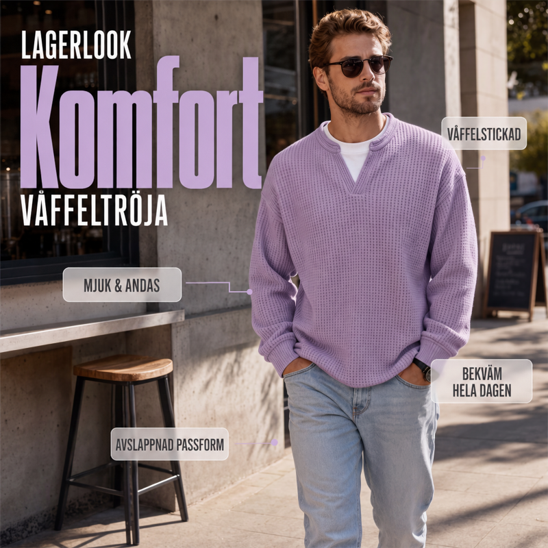 Man i sjalviolett våffelstickad topp och ljusa jeans går utomhus på en gata, med solglasögon och handen i fickan. 1