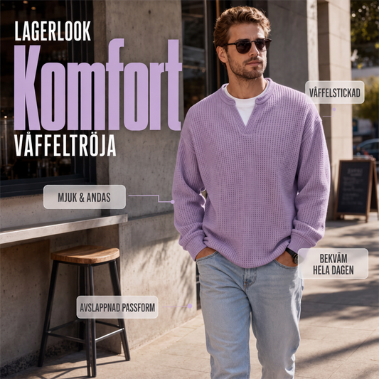 Man i sjalviolett våffelstickad topp och ljusa jeans går utomhus på en gata, med solglasögon och handen i fickan. 1