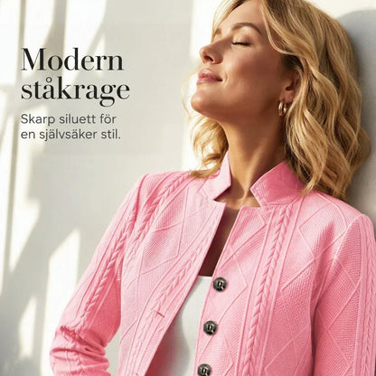Närbild på rosa blazer med stolpkrage och flätmönster, bärd av en kvinna som lutar huvudet bakåt mot en vägg. 19