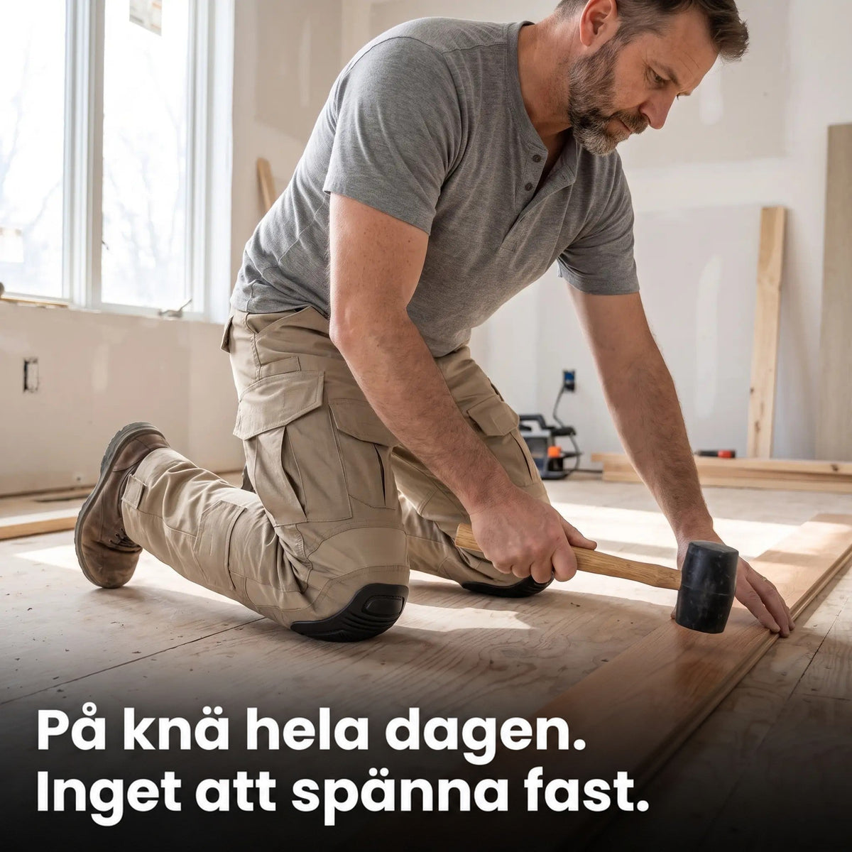 Man i beige arbetsbyxor knäböjer på ett golv under renovering och lägger trägolv med en gummiklubba, knäskydden mot golvet. 3