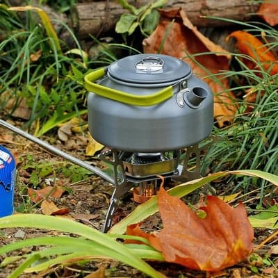 Kompakter Campingkocher mit grauem Aluminiumkessel und grünem Griff im Herbstlaub.