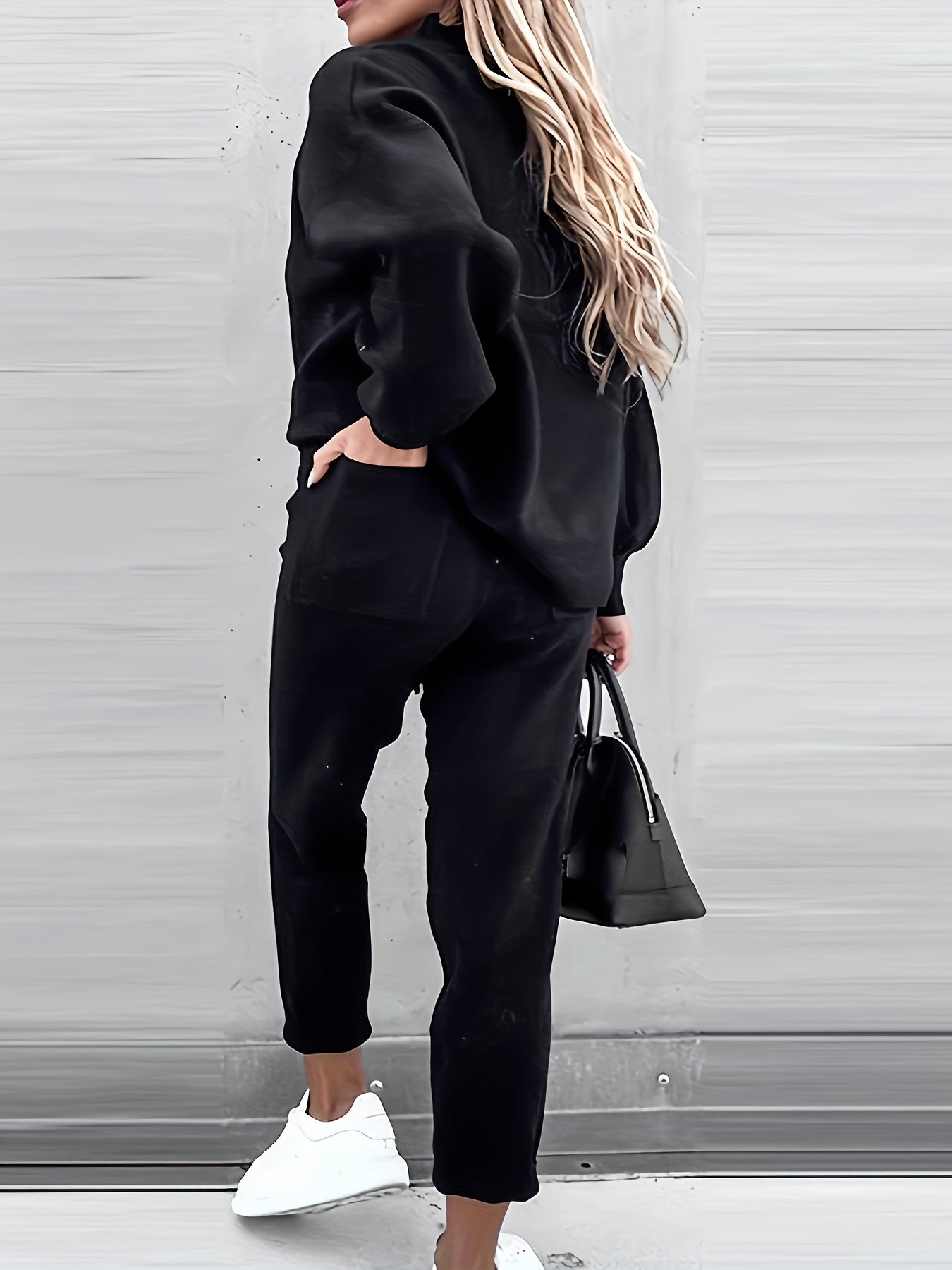 Frau in schwarzem Jogginganzug mit Tasche und weißen Sneakers, lässige Mode, Rückansicht.