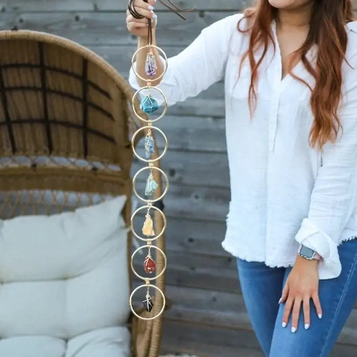 Frau hält Chakra-Wanddeko mit sieben bunten Kristallen, Boho-Stil, hängend, Holz-Hintergrund.