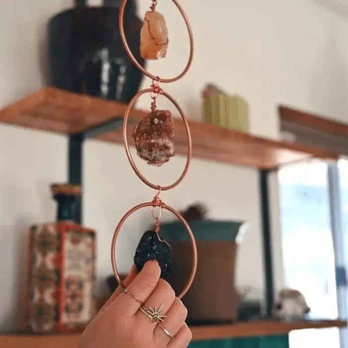 Hand hält Chakra-Dekoration mit Kristallen, Kupferringe, spirituelle Wanddekoration, Boho-Stil.