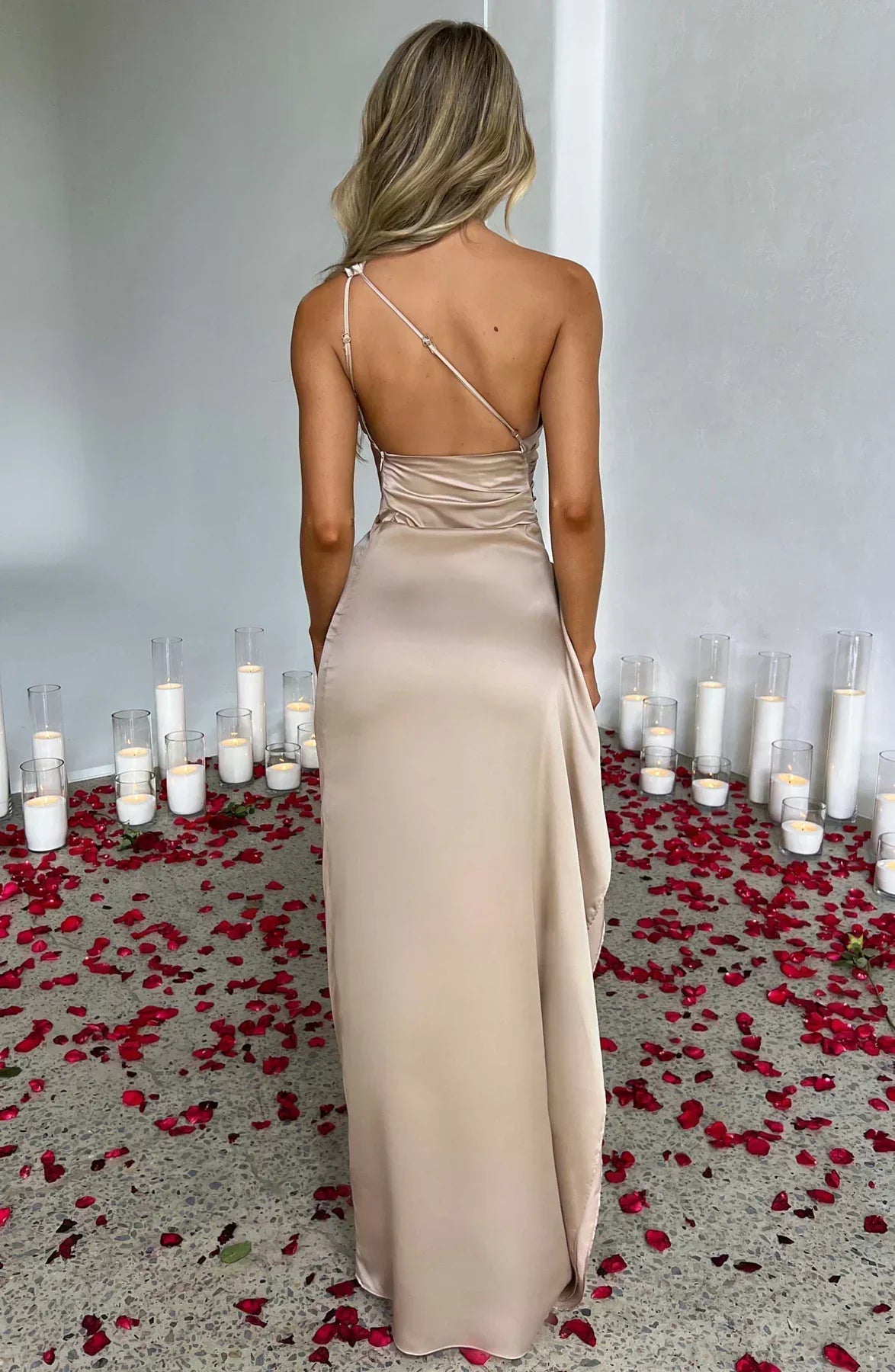 Frau in champagnerfarbenem Satin-Maxikleid, umgeben von Kerzen und Rosenblättern.