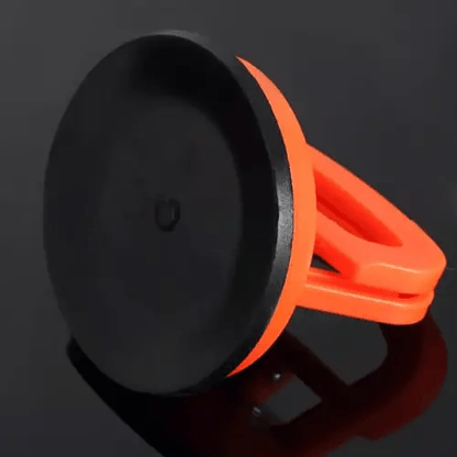 Orange sugkopp sedd från undersidan med den släta svarta gummiskivan som fäster mot bilplåten, mot mörk glänsande bakgrund. 3