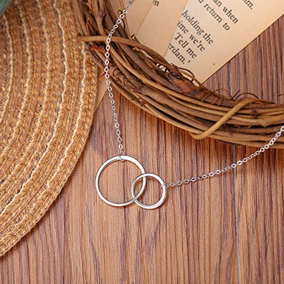 Silberne Halskette mit zwei ineinander greifenden Ringen auf Holztisch, eleganter Schmuck.