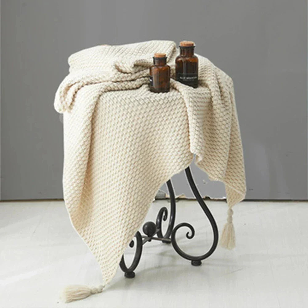 Beigefarbene Strickdecke auf Metallhocker mit braunen Glasflaschen, Wohnaccessoires, gemütlich.