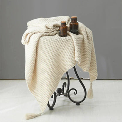 Beigefarbene Strickdecke auf Metallhocker mit braunen Glasflaschen, Wohnaccessoires, gemütlich.
