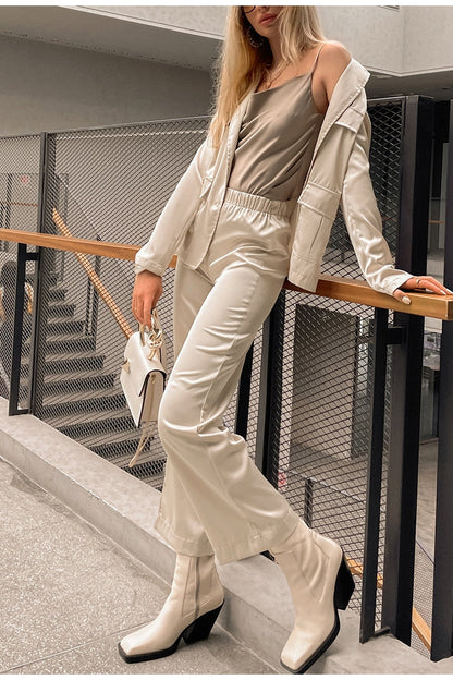 Frau in cremefarbenem Lederoutfit mit Tasche und Stiefeln auf modernem Balkon.