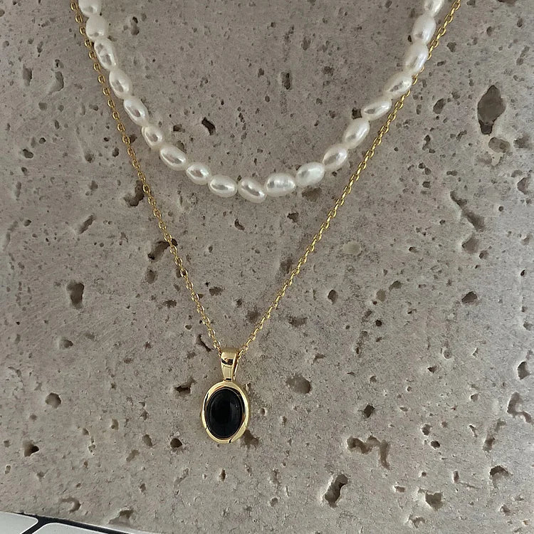 Goldene Halskette mit schwarzem Anhänger und Perlenkette auf Betonhintergrund.