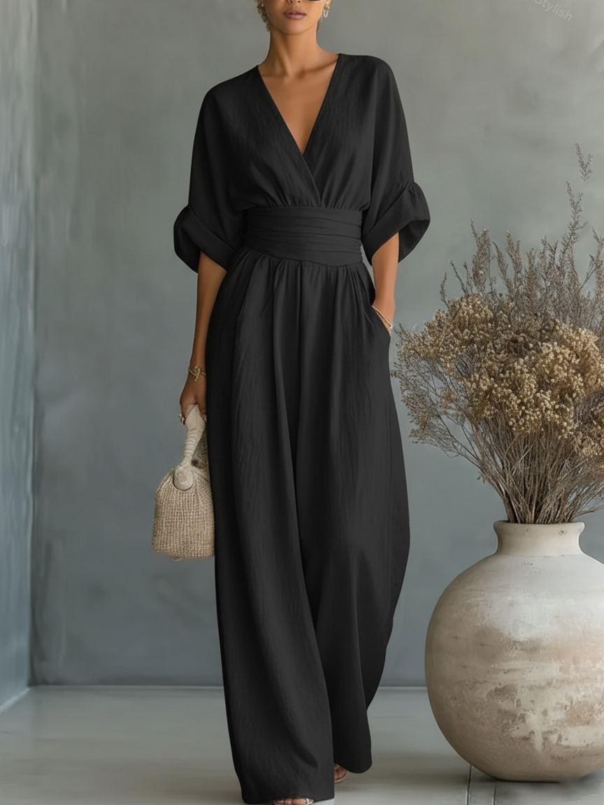 Kvinna i svart jumpsuit med V-ringning, uppvikta ärmar och vida ben, med en flätad väska 4