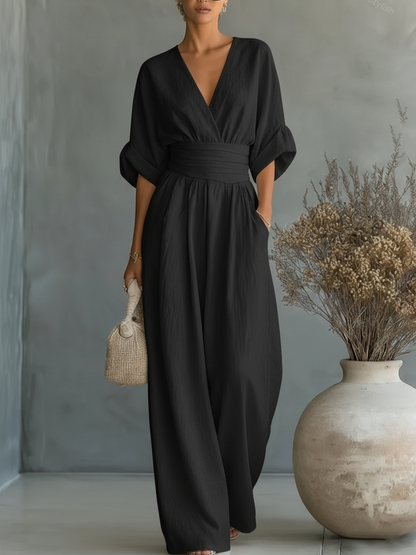Kvinna i svart jumpsuit med V-ringning, uppvikta ärmar och vida ben, med en flätad väska 4