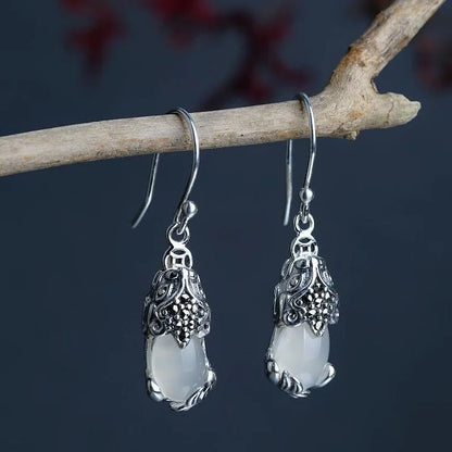 Silberne Ohrringe mit weißem Opal, filigranes Design, hängend an Ast, Schmuckfotografie.