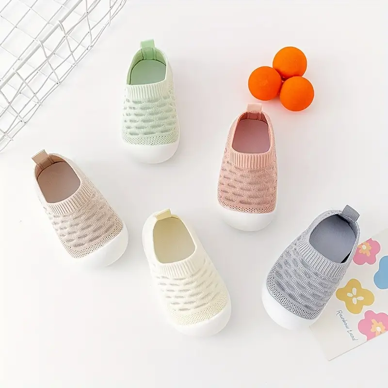 Fünf Paar Baby-Sneaker in Pastellfarben auf weißem Hintergrund mit Orangen und Blumenkarte.
