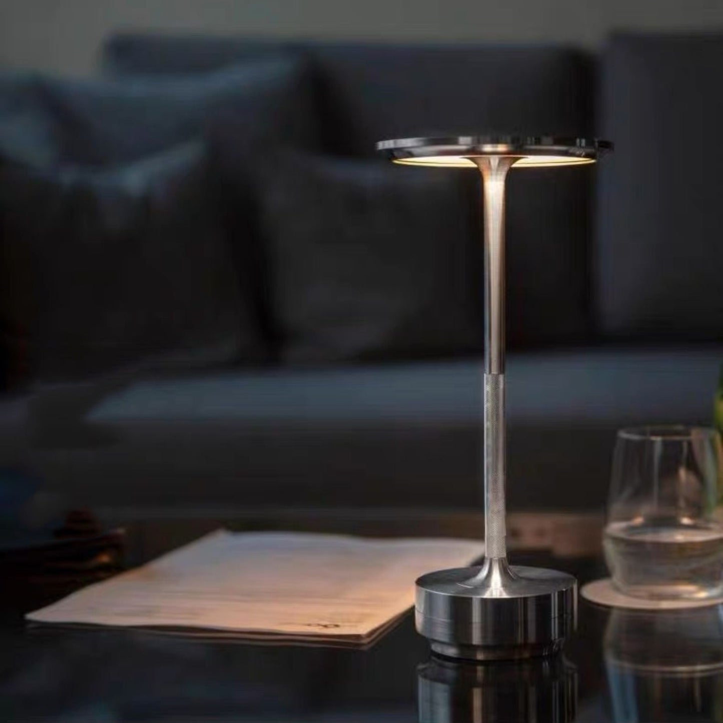 Moderne LED-Tischlampe aus Metall, dimmbar, silber, auf Glastisch im Wohnzimmer.