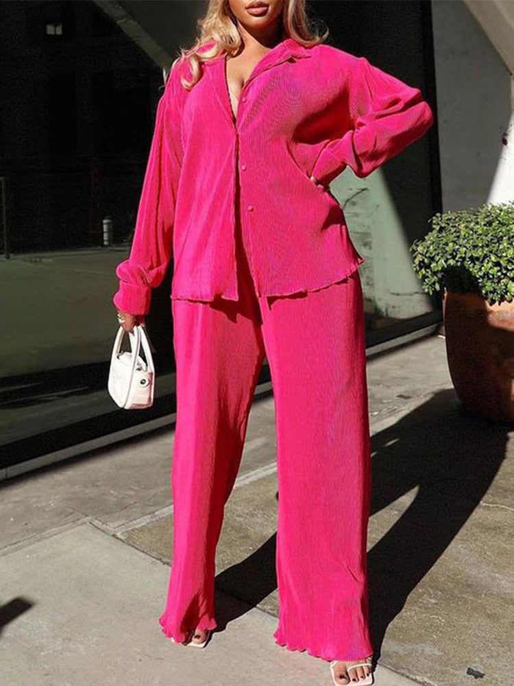 Frau in pinkem Cordanzug mit weißer Handtasche, modisch, urbaner Stil, sonniger Tag.