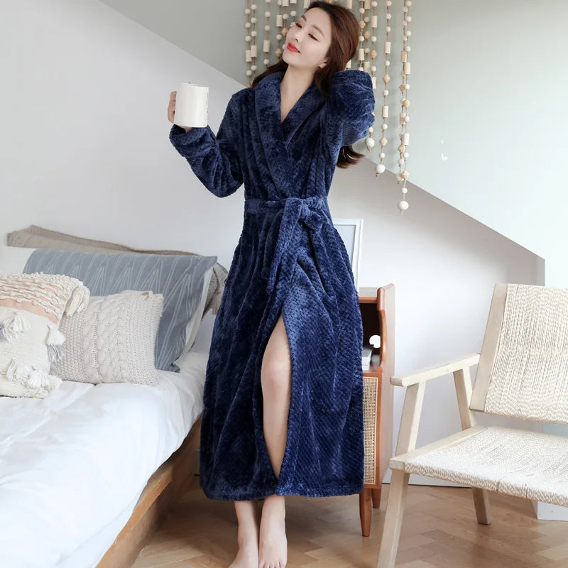 Frau im blauen Fleece-Bademantel mit Kaffeetasse im Schlafzimmer, gemütliche Morgenroutine.