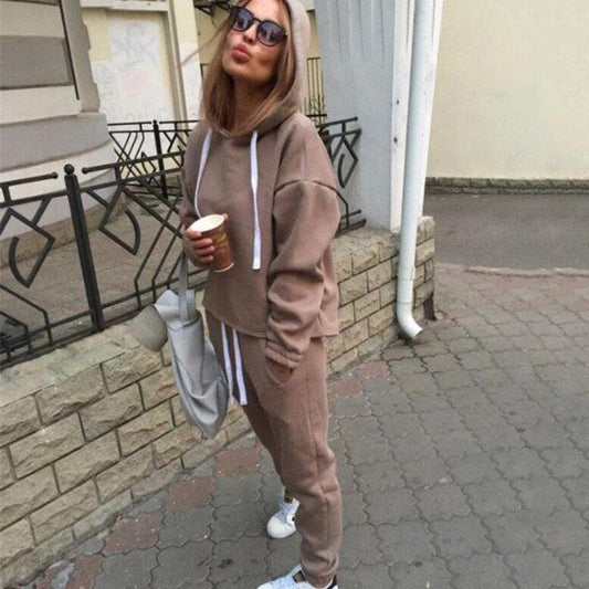 Frau in braunem Hoodie und Jogginghose, hält Kaffeebecher, lässige Straßenmode.
