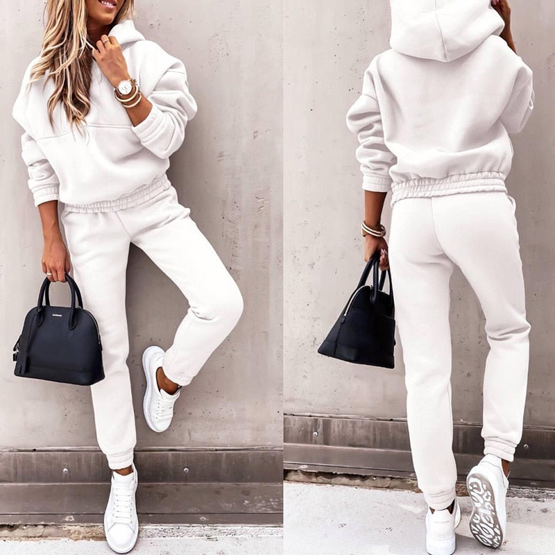 Frau in weißem Hoodie und Jogginghose, schwarze Handtasche, weiße Sneaker, lässige Mode.